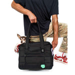 Man holding a black Just Fred Companion dpg bag with a chihuahua dog peeking out, wearing a black shirt and camouflage pants.