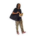 Man holding a black Just Fred Subway tote dog bag with a Corgi dog peeking out, wearing camouflage pants and red sneakers on a white background.