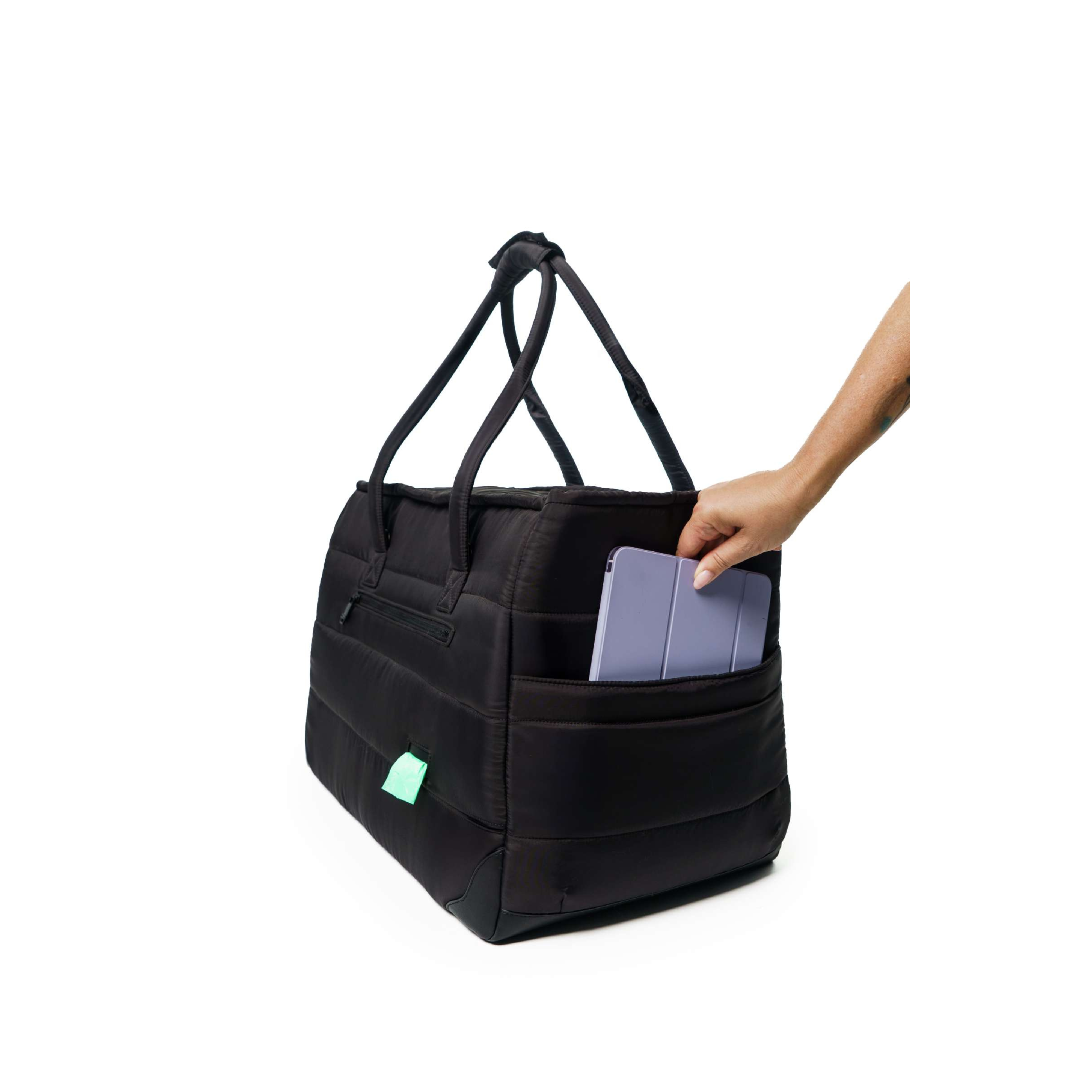 Black Just Fred Subway tote pet dog carrier bag with a hand placing a tablet inside the side pocket, on a white background