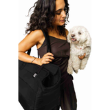 Woman holding a black Just Fred Subway dog bag carrier while holding a white Bichon Frise dog on a white background