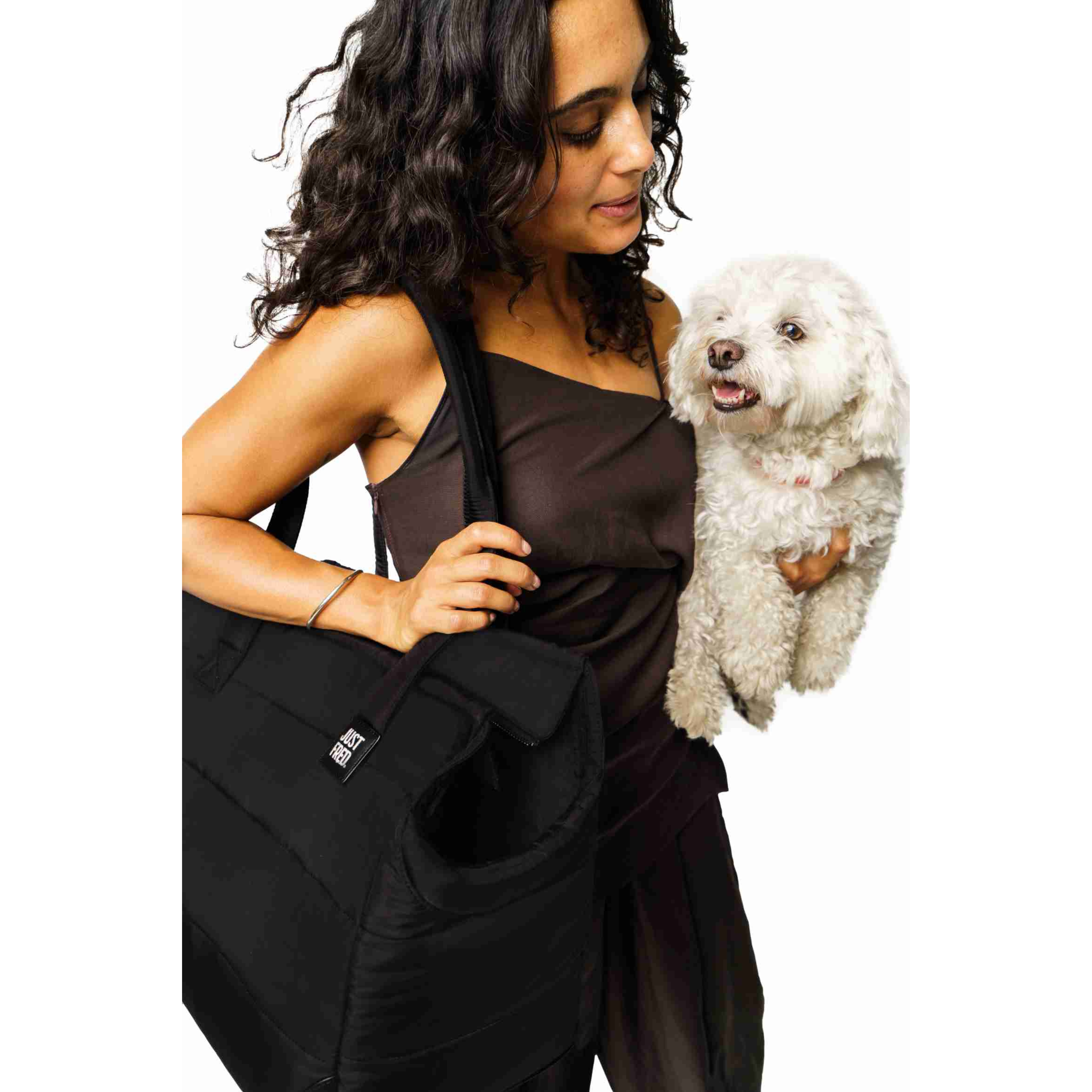 Woman holding a black Just Fred Subway dog bag carrier while holding a white Bichon Frise dog on a white background
