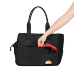 Woman's arm putting a leash into the side pocket of the black Just Fred x Fem World by Ally Lindsay Weekend Tote dog pet carrier, on a white background