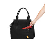 A woman's arm places a red Just Fred leash into the back zipped pocket of a black Just Fred Destination Tote, on a white background.