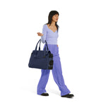 A Woman wearing a blue top and purple pants holding a Just Fred Navy Destination Tote showing breathable mesh window, on a white background 