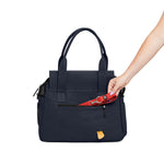 A woman's arm places a red Just Fred leash into the back zipped pocket of a Just Fred Navy Destination Tote, on a white background 